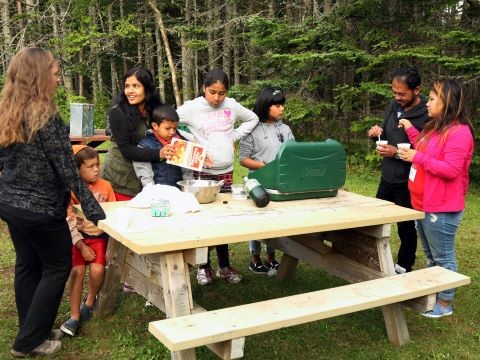 a group of people gathered around a picnic table cooking over a Coleman stove.