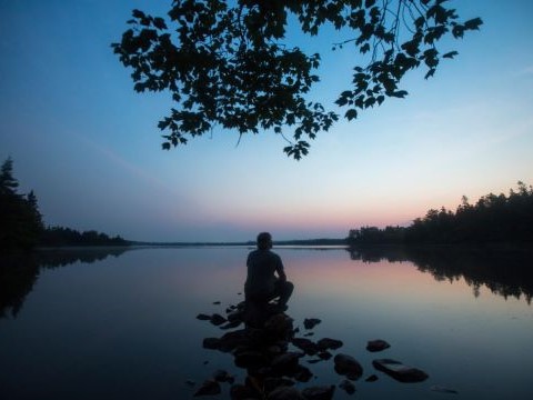 a person sitting on a rock overlooking the lake as the sun sets.