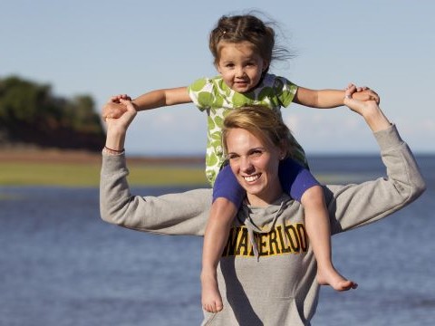 a young kid sitting on the shoulders of a person while wading in the water.