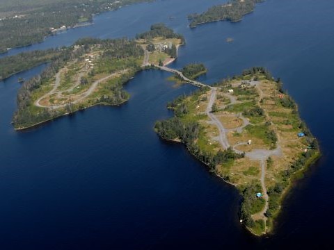 aerial photograph of a small island surrounded by water with a few campsites occupied by colourful tents and campers.