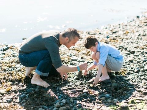 Two people in bare feet on the shoreline looking at the various rocks and shells.