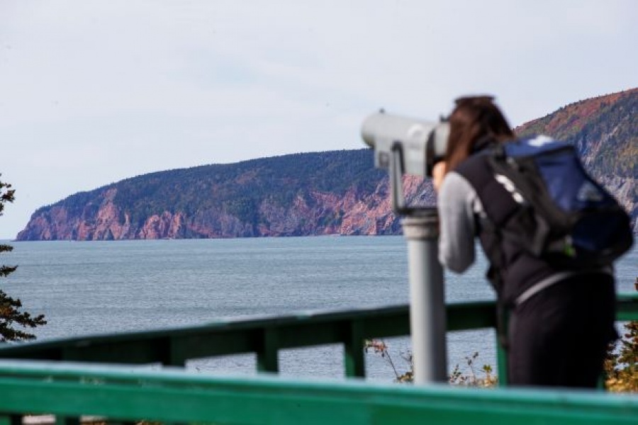 A woman looks through binoculars at the cliffs at Cape Chignecto.