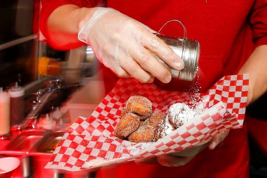 close up photo of a person sprinkling sugar on donuts