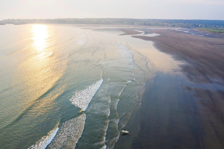 Aerial image of Mavillette Beach with a surfer wading into the waves. 